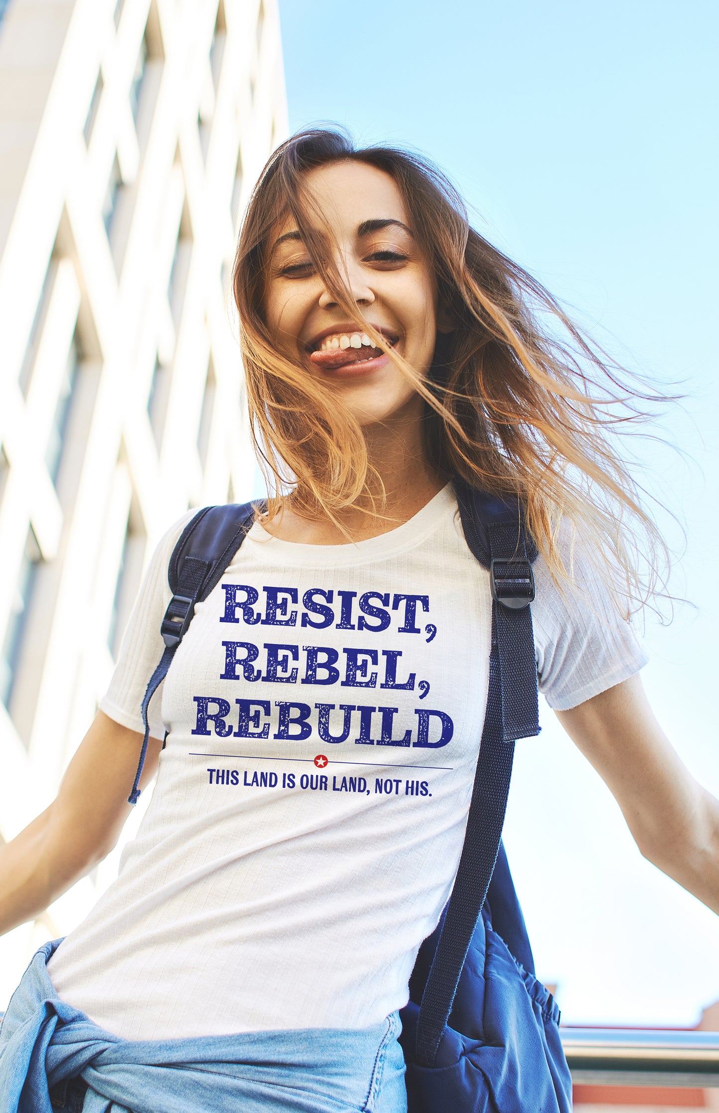 Woman wearing a t-shirt with 'Resist, Rebel, Rebuild' text outdoors.