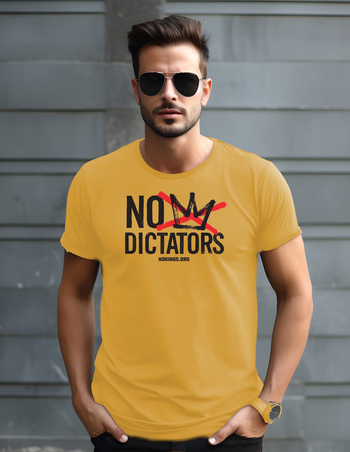 Man wearing a yellow t-shirt with 'No 
 Dictators' text against a gray wall.