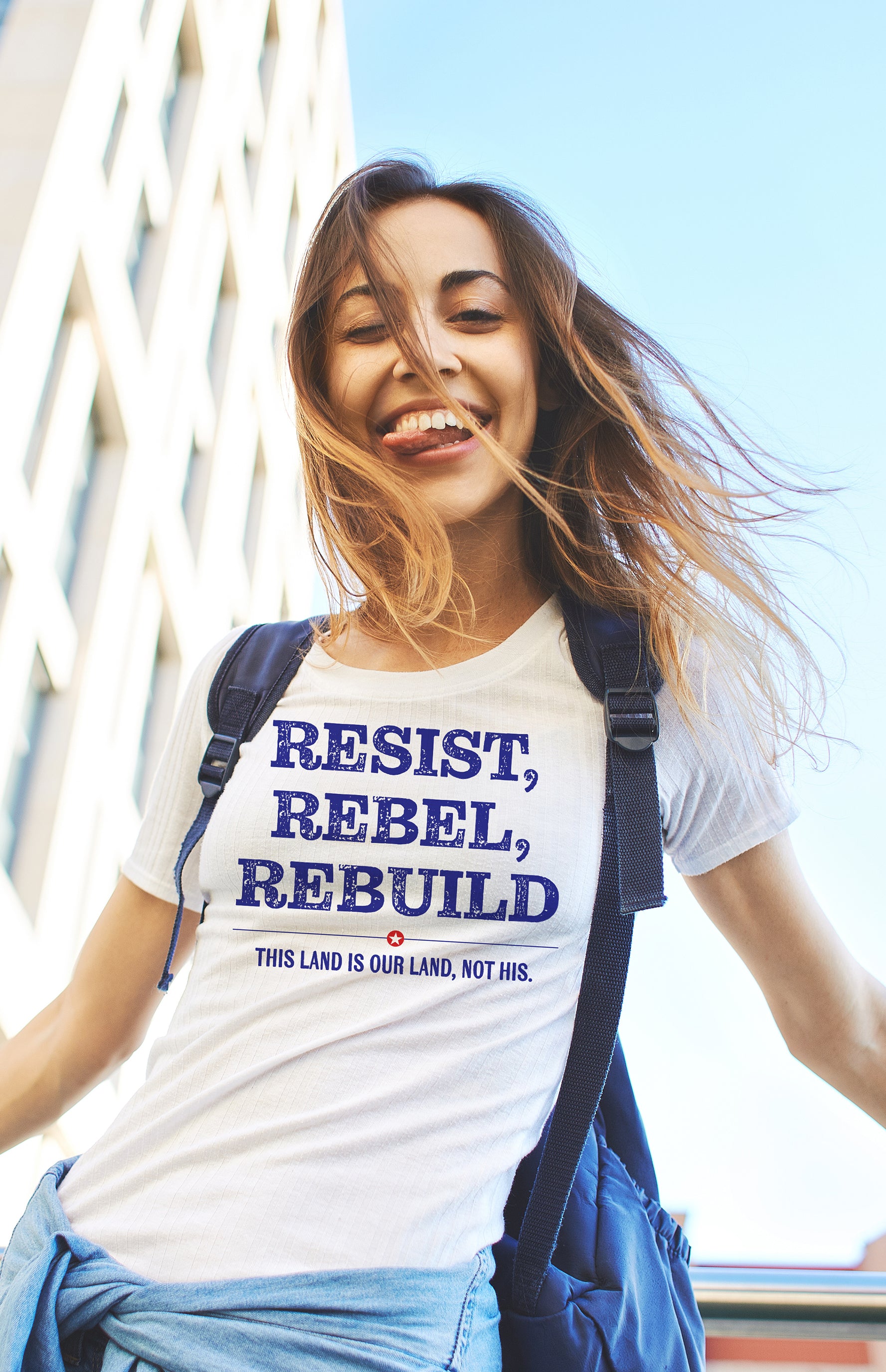 Woman wearing a t-shirt with 'Resist, Rebel, Rebuild' text outdoors.