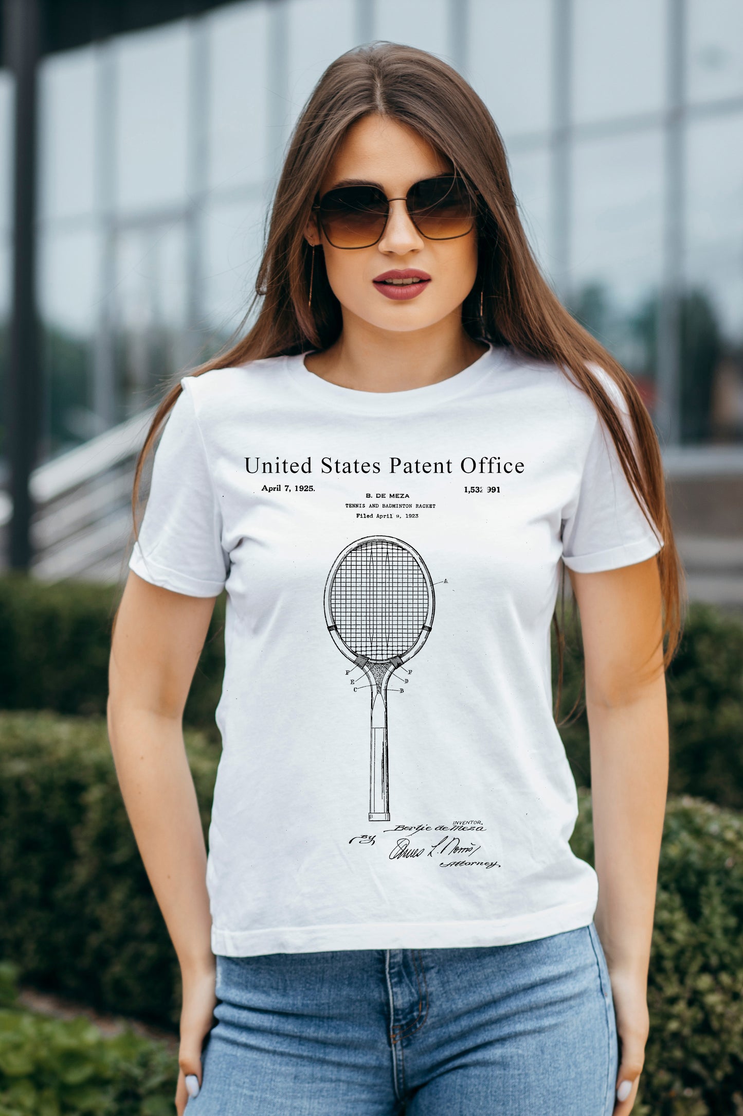 Woman wearing a white t-shirt with a tennis racket design and text, standing outdoors.