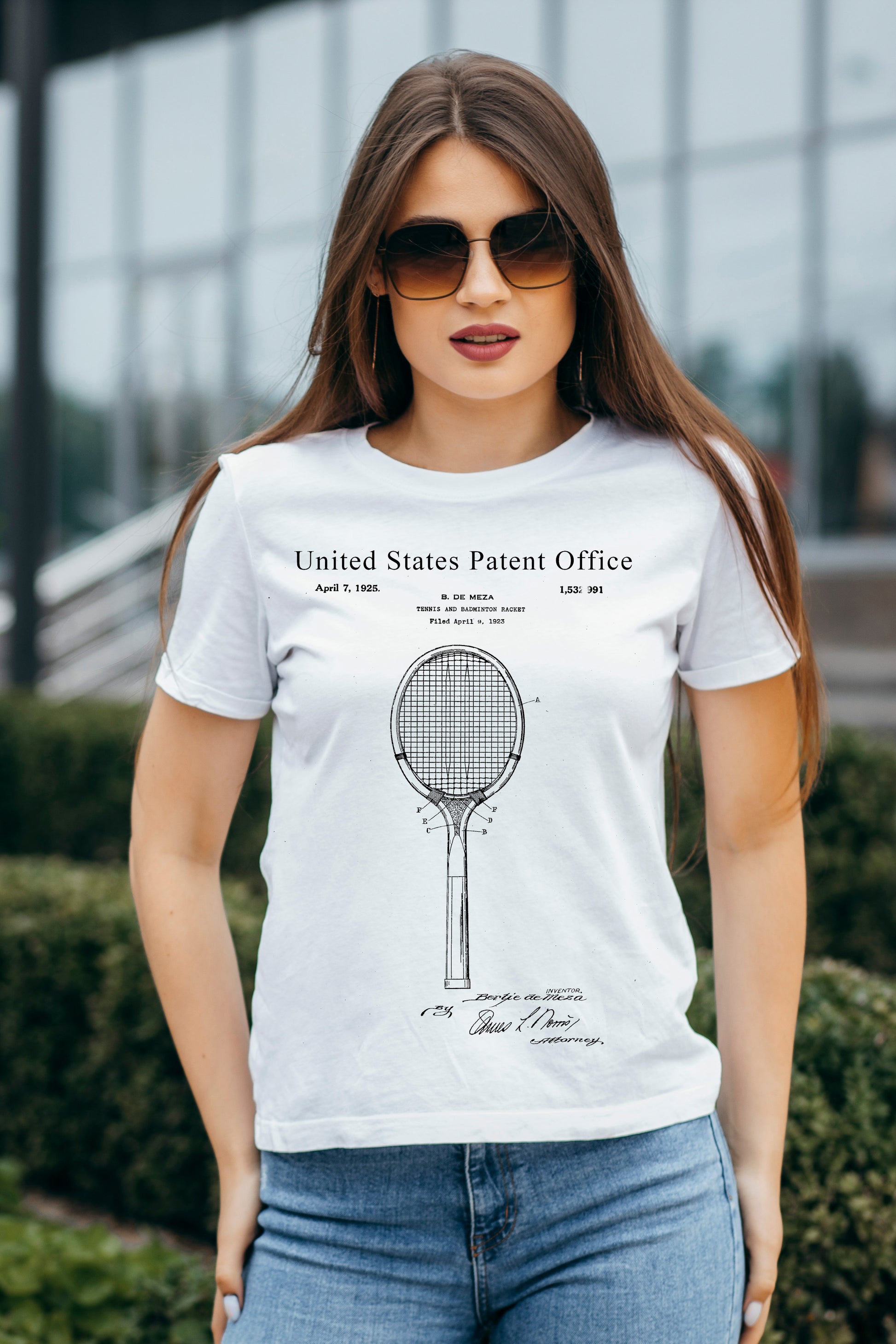 Woman wearing a white t-shirt with a tennis racket design and text, standing outdoors.